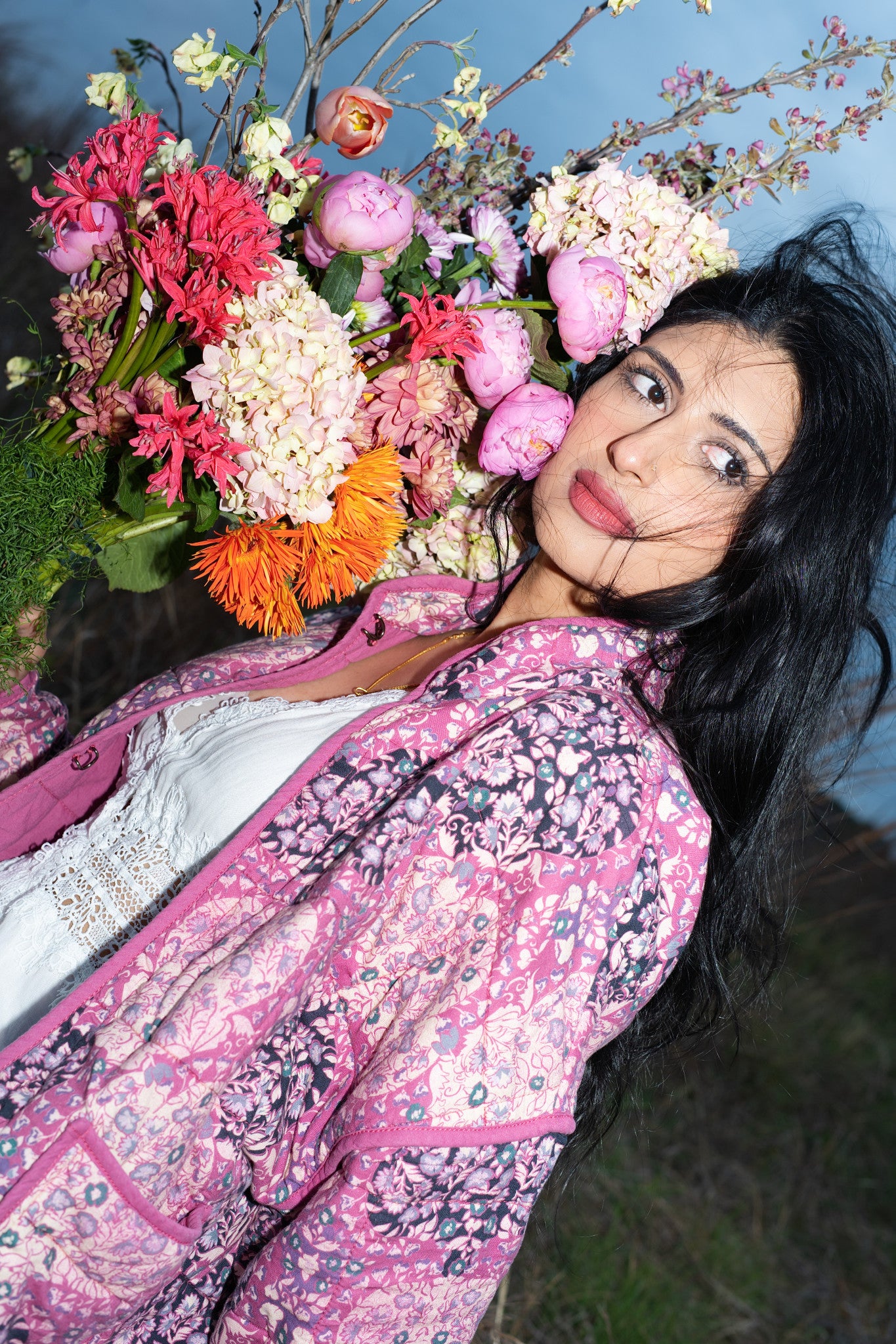 Woman in a floral dress surrounded by flowers against a blue background Austin Texas