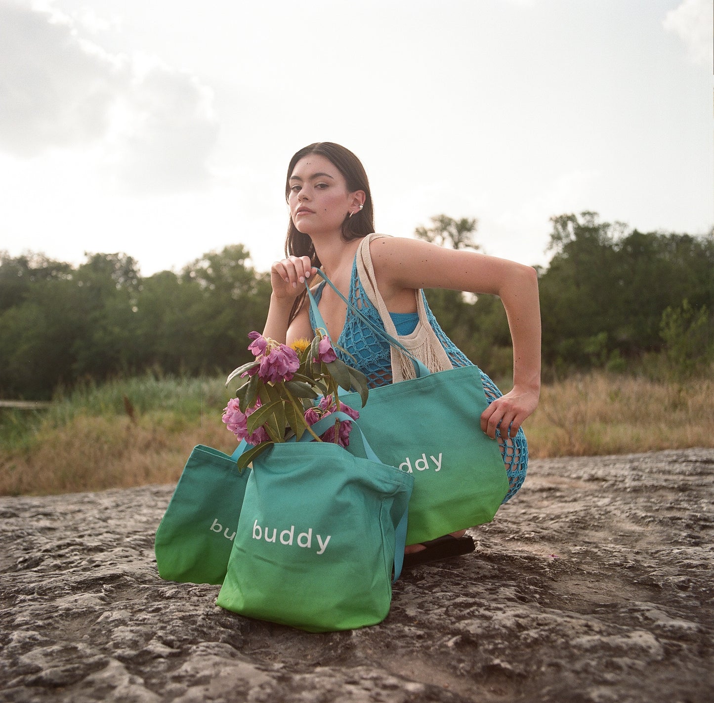 Woman holding flowers with ombre green 'buddy' bags in a natural setting