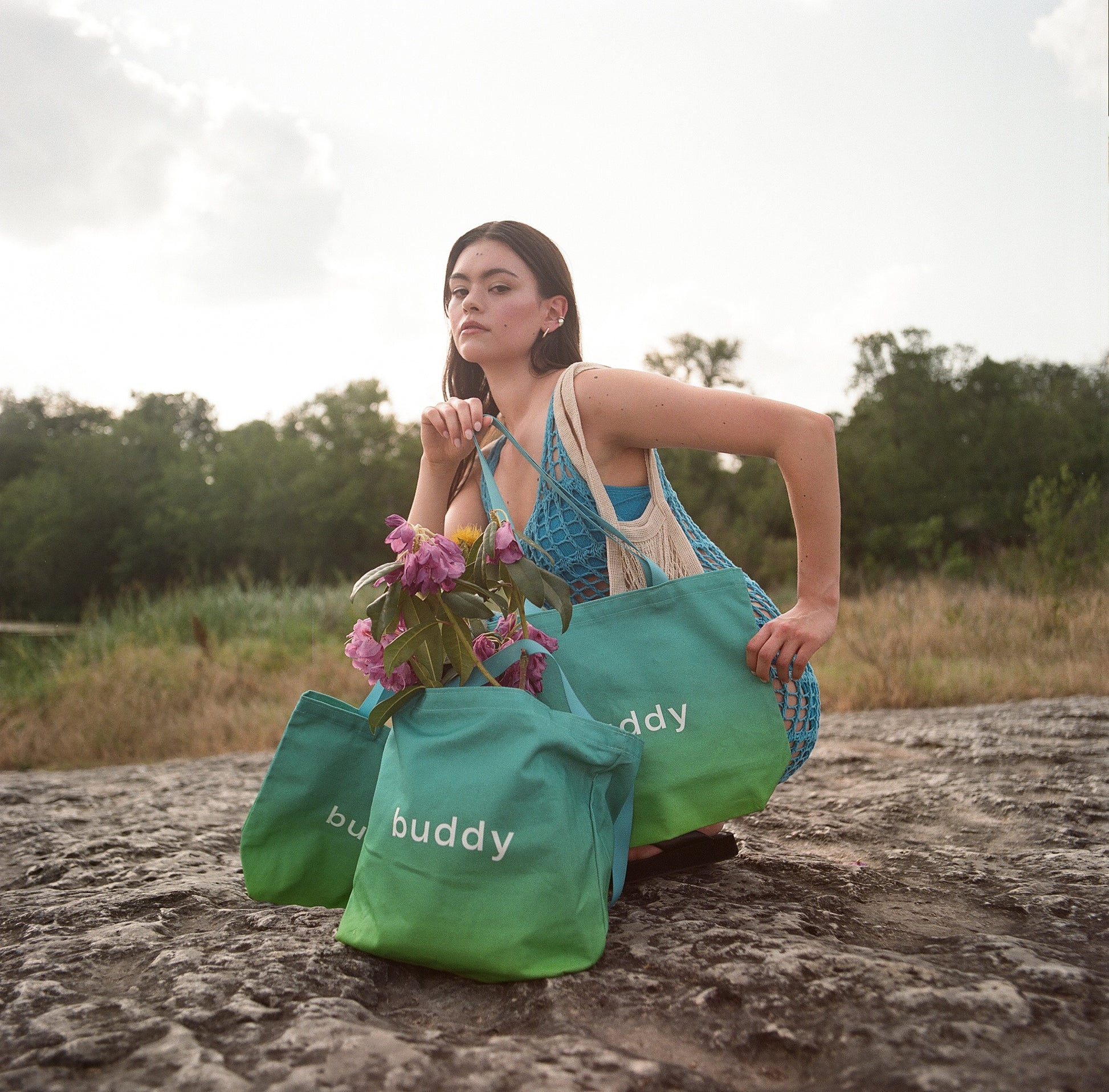 Woman holding flowers with ombre green 'buddy' bags in a natural setting