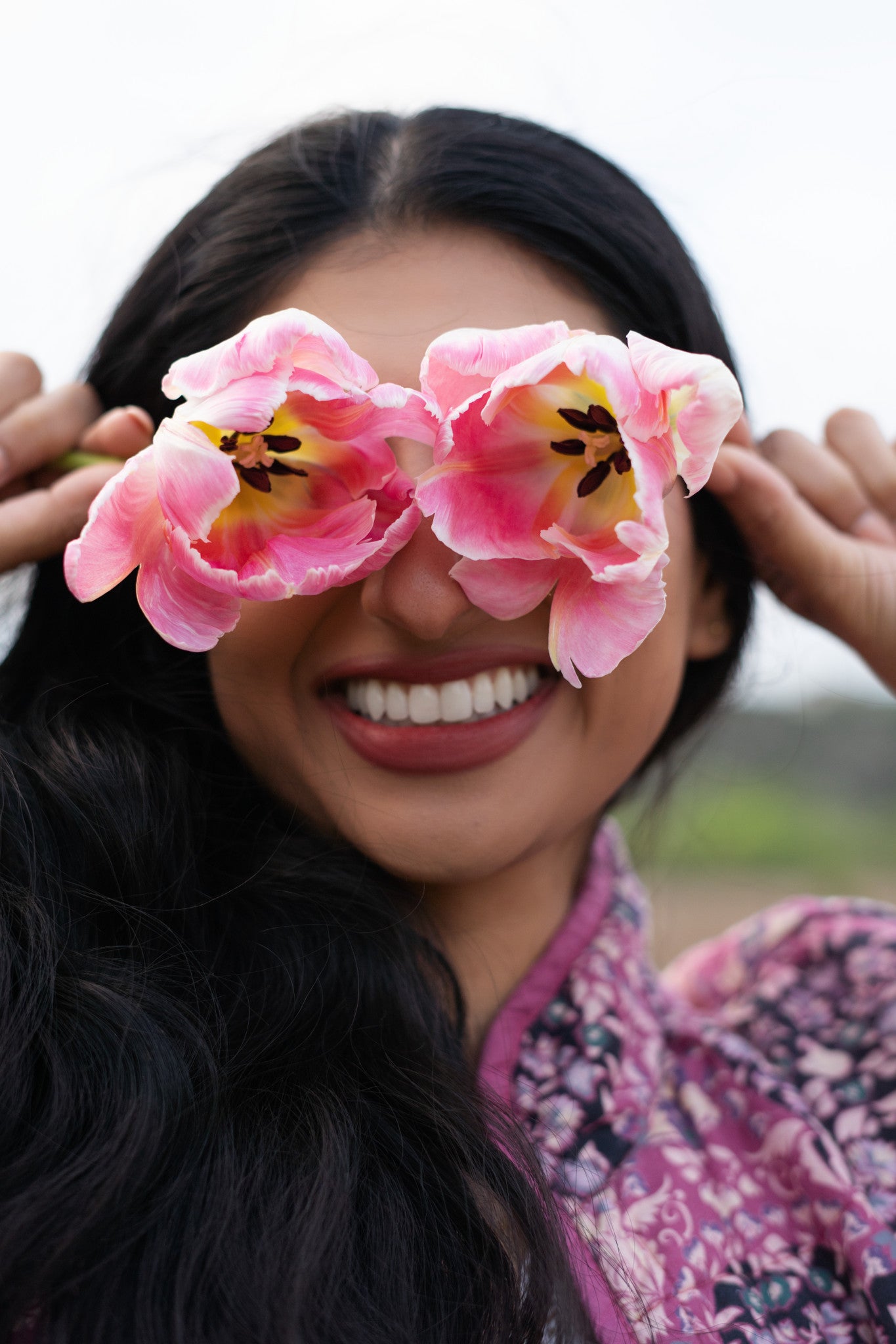 Woman holding two flowers over her eyes and smiling