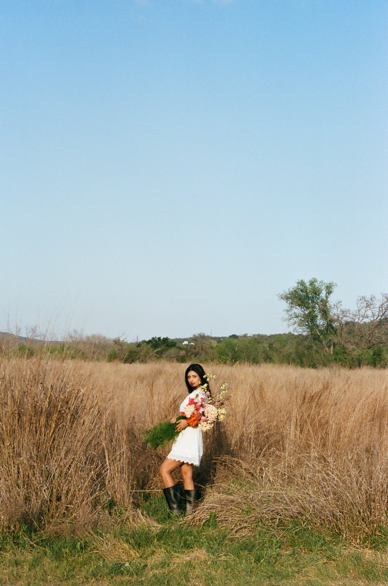 Woman standing in a field of tall brown grass with a clear blue sky in Austin Texas.